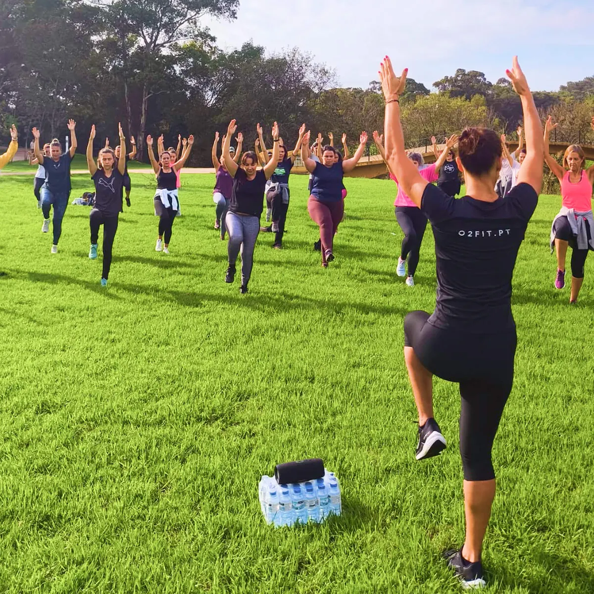 Treinadora O2Fit de costas a guiar o grupo em equilíbrio no relvado do Jamor